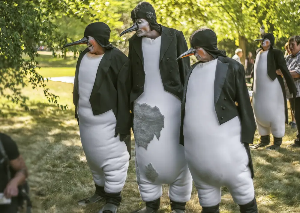 Mehrere Personen in Pinguinkostümen mit Frack und Schnabelmaske bei einer Outdoor-Veranstaltung im Grünen, im Rahmen eines Aktionstags zum Artenschutz.